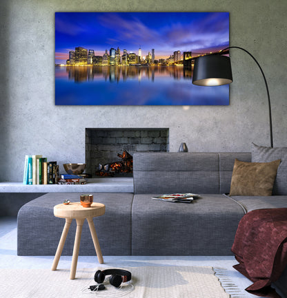 A glossy acrylic art print featuring a cityscape at dusk, displayed above a grey sofa in a room with a modern decor.